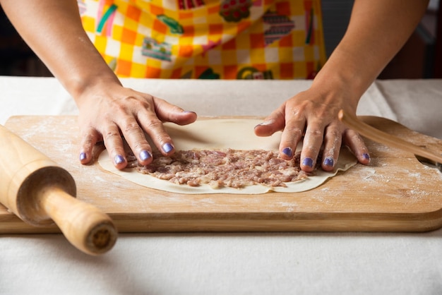 Women's hands making Azerbaijani dish gutab on wooden board. 