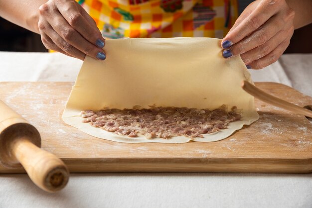 Women's hands making Azerbaijani dish gutab on wooden board. 