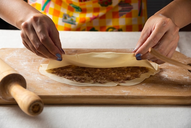 Women's hands making Azerbaijani dish gutab on wooden board. 