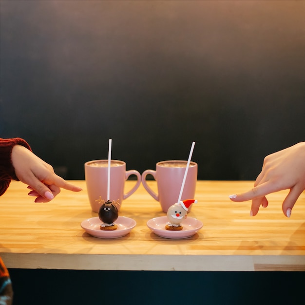 Women show with their fingers at pretty sweet balls with Christmas design standing on pink plates