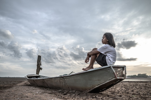 Foto gratuita le donne si siedono abbracciando le ginocchia su una barca da pesca e guardano il cielo sulla terra ferma e il riscaldamento globale