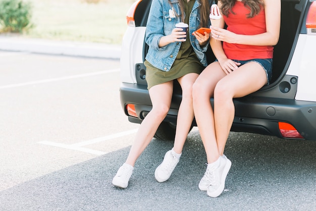 Free photo women sitting on car trunk in parking