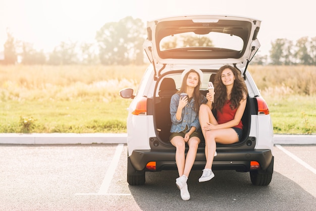 Women sitting on car trunk with ice cream