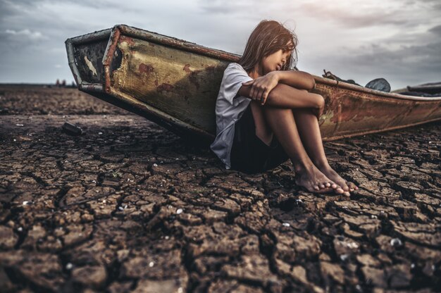 Women sitting hugging their knees, bent on the dry soil and there were fishing boats.