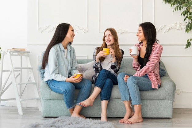 Women sitting on sofa and chatting holding cups in hand