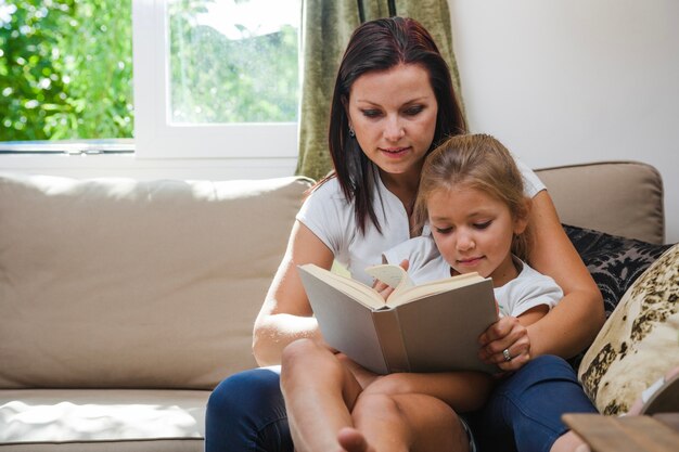 Women sitting on sofa reading book together