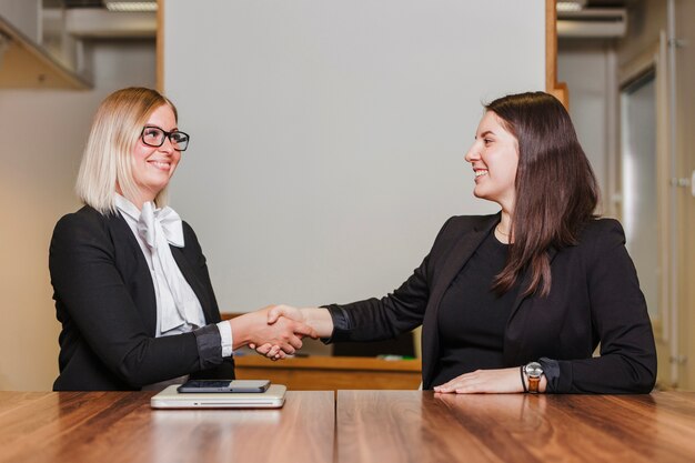 Women sitting at table shaking hands smiling