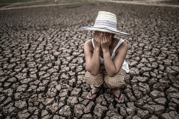 Free photo women sitting on their hands, closed their faces on dry ground in a warming world.