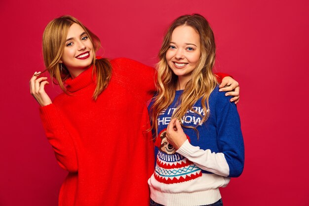 Women standing in stylish winter warm sweaters on red wall