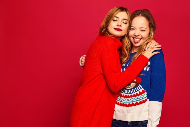 Women standing in stylish winter warm sweaters on red wall