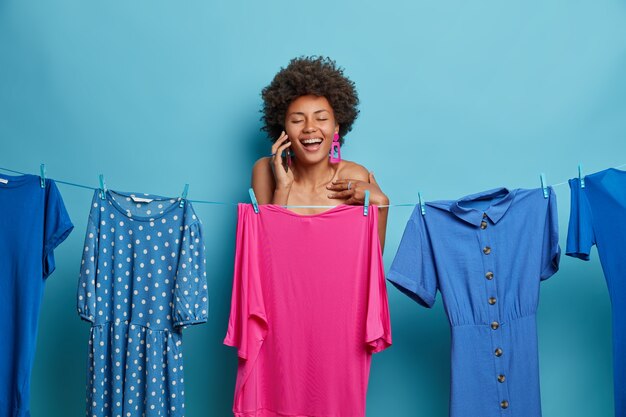 여성, 스타일 및 패션 개념. 기뻐하는 성인 아프리카 계 미국인 여성이 전화 통화를하고 핑크색 이브닝 드레스 뒤에 벌거 벗은 포즈를 취합니다.