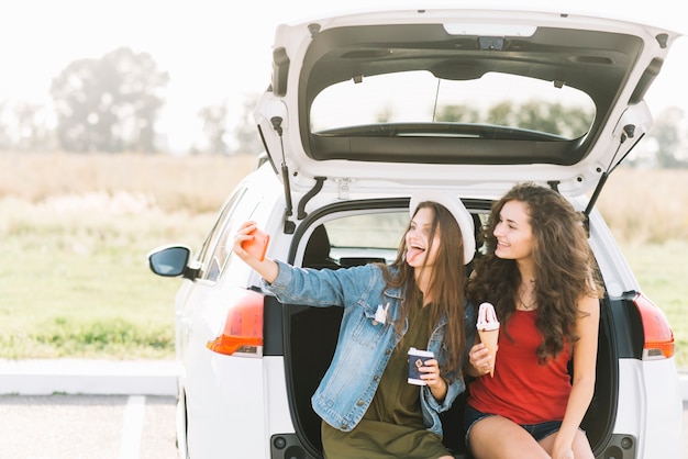 Women taking selfie on car trunk
