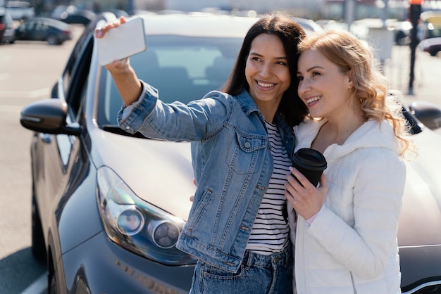 women taking a selfie next to a car