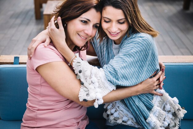 Women tenderly hugging on sofa