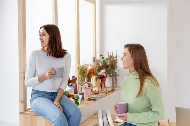 Женщины в цветочном магазине держат кружки с кофе