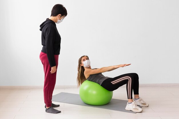 의료 마스크를 착용하는 동안 피트니스 공을 훈련하는 여성
