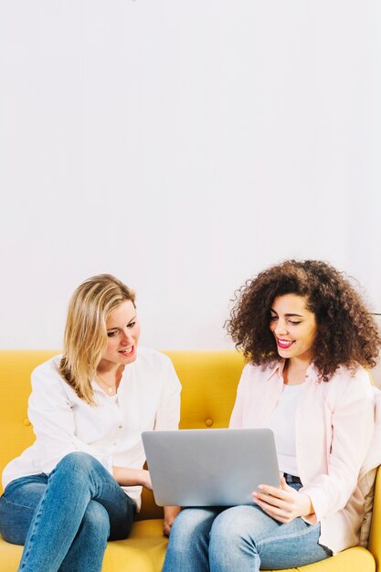 Women using laptop on yellow couch