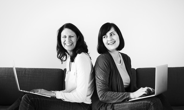 Women using laptops on the sofa together