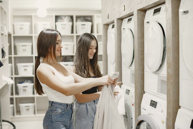 Женщины стирают белье в стиральной машине. Молодые девушки готовы постирать одежду. Интерьер, концепция процесса стирки