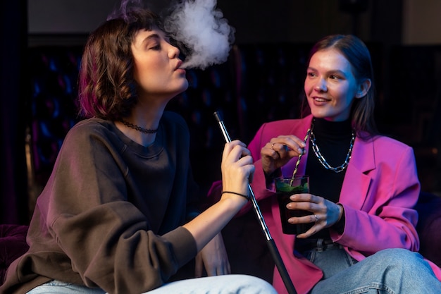 Women vaping from a hookah indoors