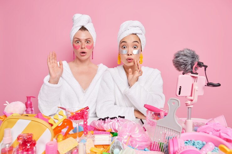 Free Photo women wear white bathrobe and towels on head give review creat video about skin care apply beauty patches pose near table with cosmetic products around.