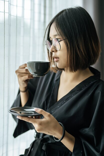 검은 가운을 입고 침실에서 커피를 나눠주는 여성.