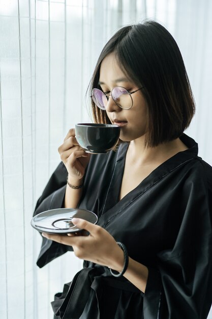 黒いローブを着て、寝室でコーヒーを渡す女性。