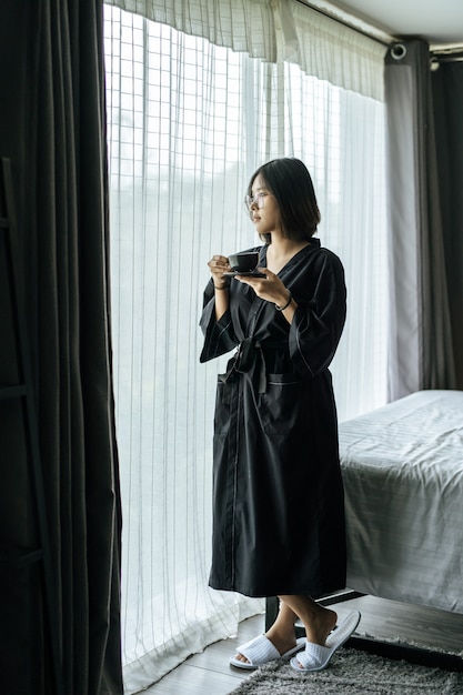 黒いローブを着て、寝室でコーヒーを渡す女性。