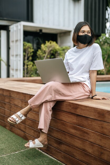 Women wearing masks and playing laptops at the poolside.