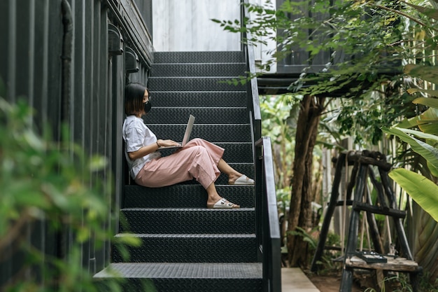 Women wearing masks and playing laptops on the stairs.