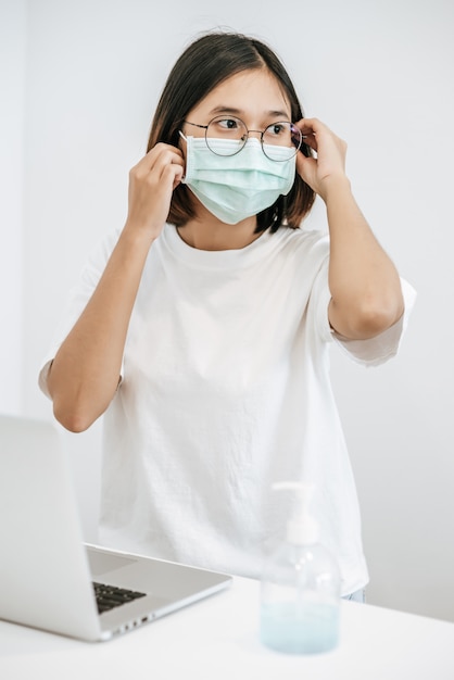 Women wearing sanitary masks have a laptop on the table and hand washing gel.