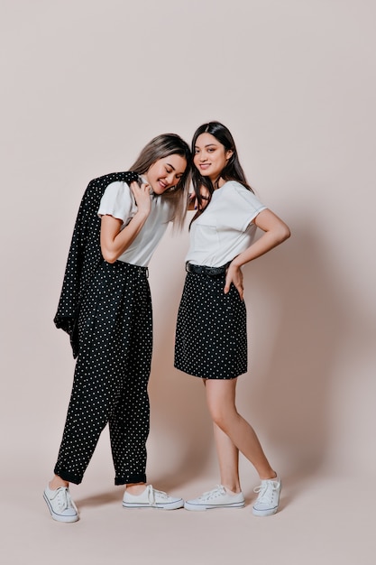 women in white T-shirts and black polka dot outfits posing on beige wall