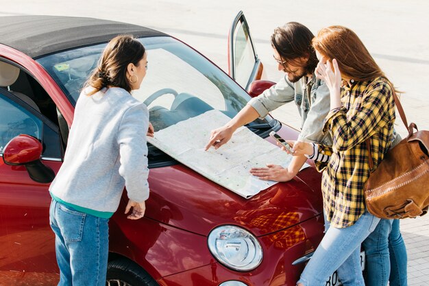 Women with backpack and smartphone near man looking at map on car hood