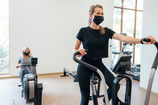 Women with medical mask during pandemic exercising at the gym