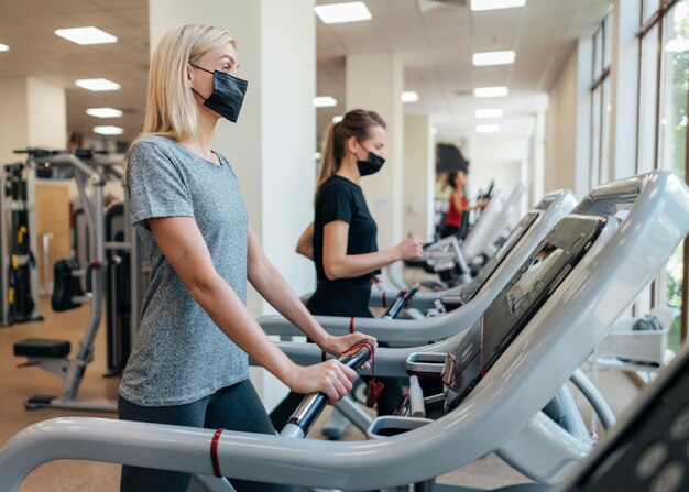 Women with medical masks using gym equipment