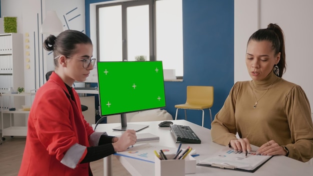 Women working together with green screen on computer. Colleagues having conversation and using monitor with isolated chroma key background and mock up template on display. Copy space