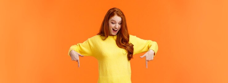 Free Photo wondered and excited amused cute redhead woman in yellow sweater pointing fingers down look bottom a