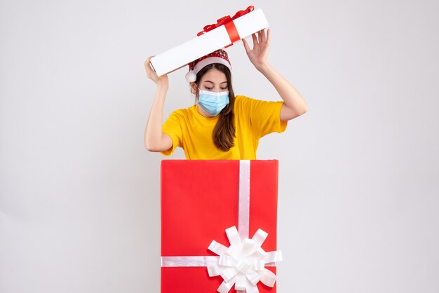 wondered girl with santa hat and mask standing behind big xmas gift on white