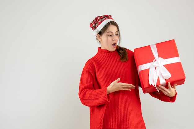 wondered girl with santa hat pointing at her xmas gift on white