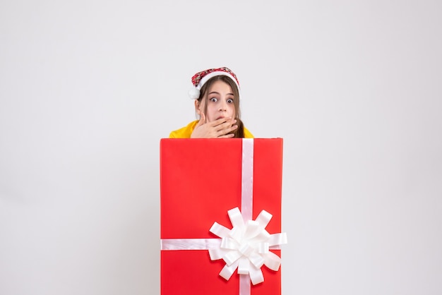 wondered girl with santa hat standing behind big xmas gift on white