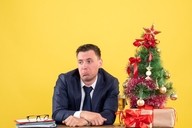 wondered man sitting at the table near xmas tree and gifts on yellow