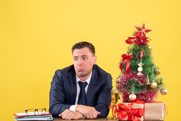 クリスマスツリーと黄色の贈り物の近くのテーブルに座っている不思議な男