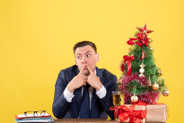 wondered man sitting at the table near xmas tree and presents on yellow