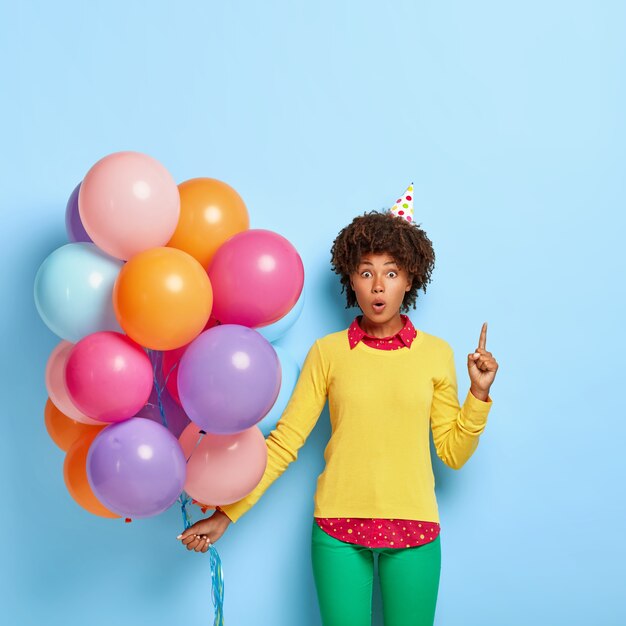 Wondered woman holds multicolored balloons while posing in a yellow sweater