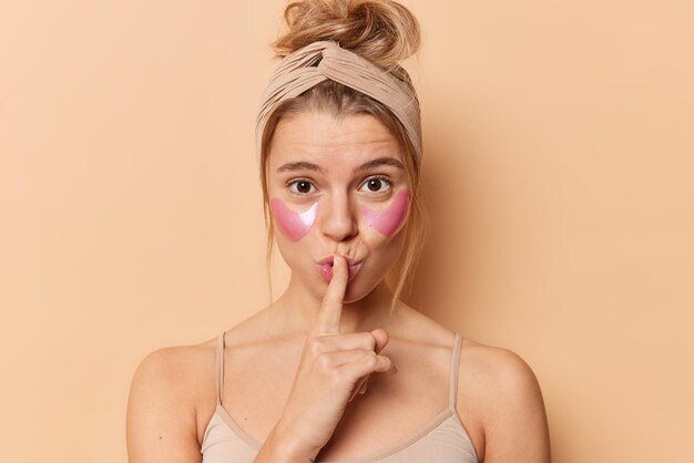 不思議な女性は、唇の上に人差し指を押して、しわを減らすために目の下にコラーゲンパッチを適用するハッシュサインを作成します。美容コンセプト