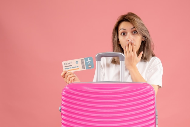 wondered young woman holding ticket behind pink suitcase