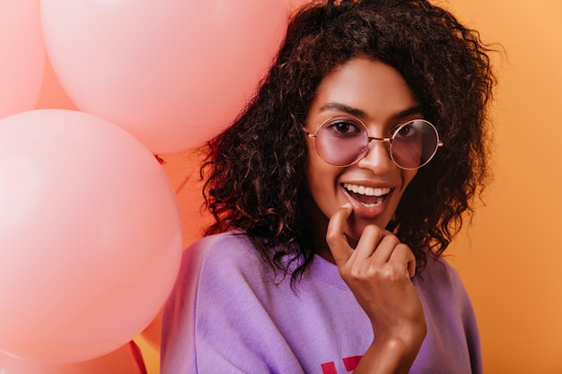 Free photo wonderful african lady playfully posing with party balloons. fascinating dark-haired girl in glasses celebrating birthday.