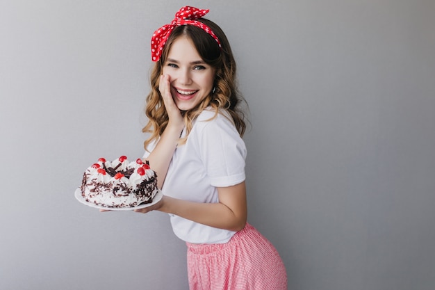 Wonderful birthday girl expressing positive sincere emotions. Indoor shot of glad european lady in vintage outfit posing with sweet cake.