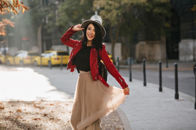 Wonderful brunette woman with charming smile playing with long skirt on city wall