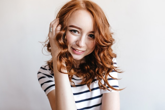 Free photo wonderful dark-eyed girl touching her ginger hair with gently smile. indoor photo of positive european lady in striped t-shirt.